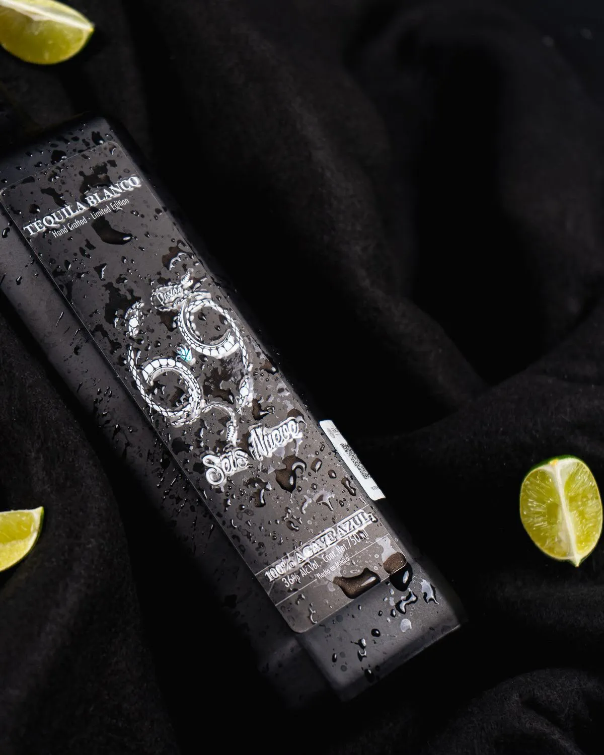 Botella Pasión 69 sobre tela negra con gotas de agua y limones